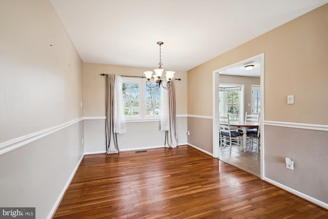 unfurnished dining area with visible vents, baseboards, an inviting chandelier, and wood finished floors