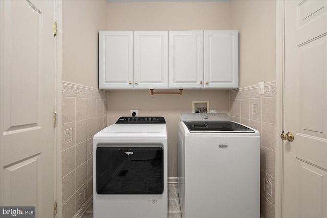 washroom with washing machine and dryer, tile walls, a wainscoted wall, and cabinet space