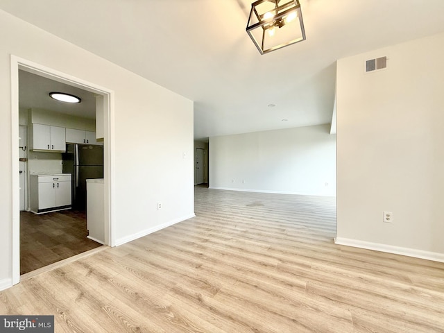 empty room with light wood finished floors, visible vents, and baseboards