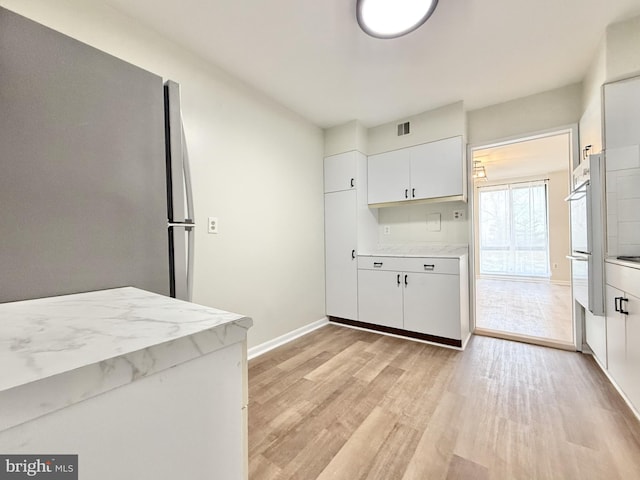 kitchen with light stone counters, light wood finished floors, stainless steel appliances, white cabinets, and baseboards