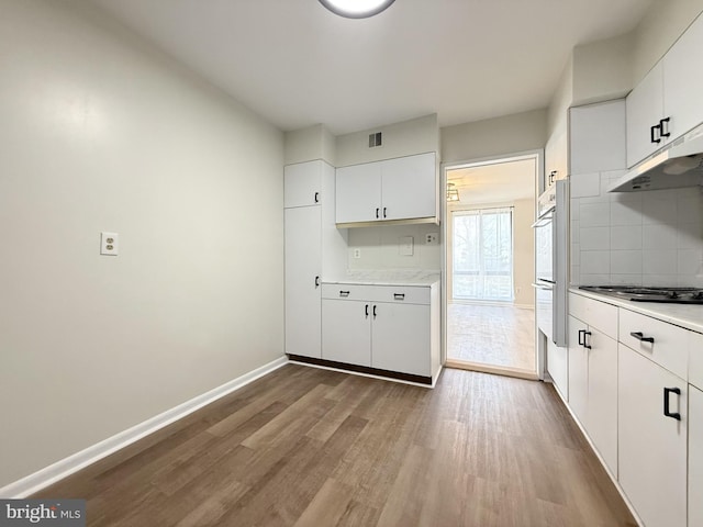 kitchen with baseboards, decorative backsplash, wood finished floors, stovetop, and under cabinet range hood