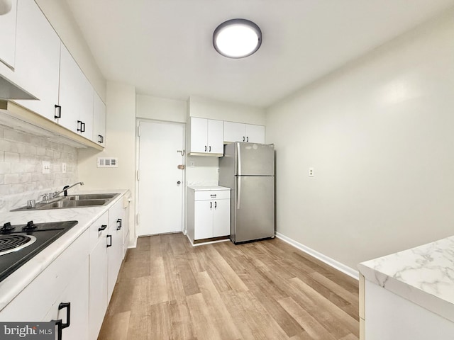 kitchen featuring light wood-style flooring, a sink, white cabinets, freestanding refrigerator, and decorative backsplash