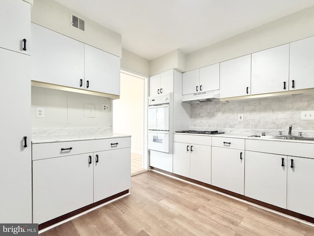 kitchen featuring light wood-style flooring, under cabinet range hood, a sink, visible vents, and tasteful backsplash