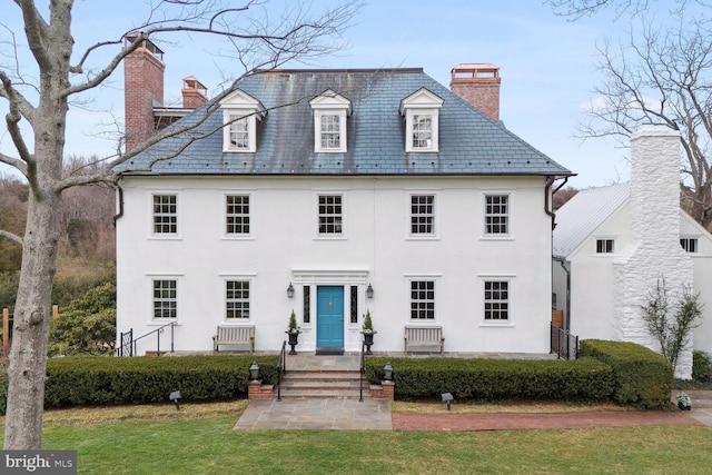 view of front of property featuring a chimney, a front yard, a high end roof, and stucco siding