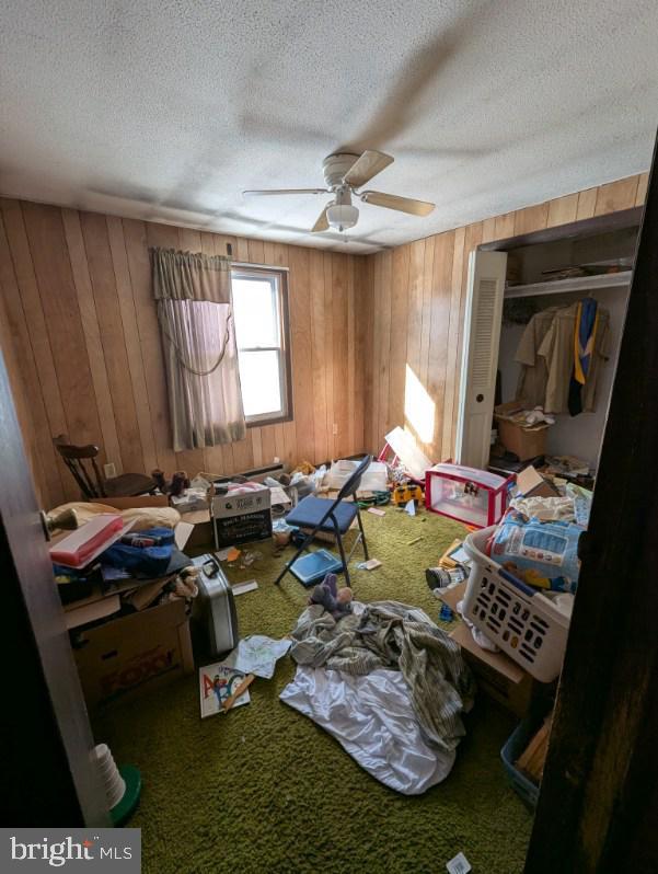 miscellaneous room featuring carpet floors, ceiling fan, a textured ceiling, and wooden walls