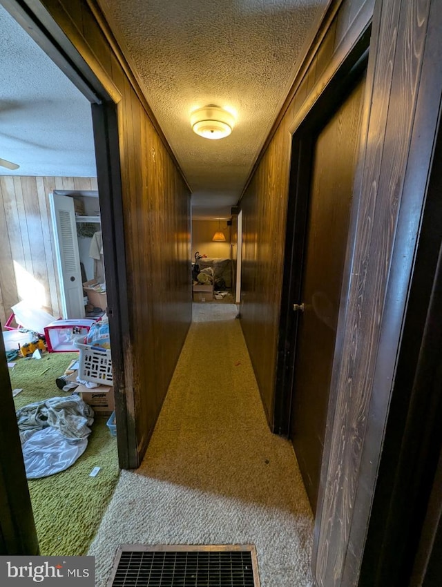 hallway featuring a textured ceiling, wood walls, and carpet flooring