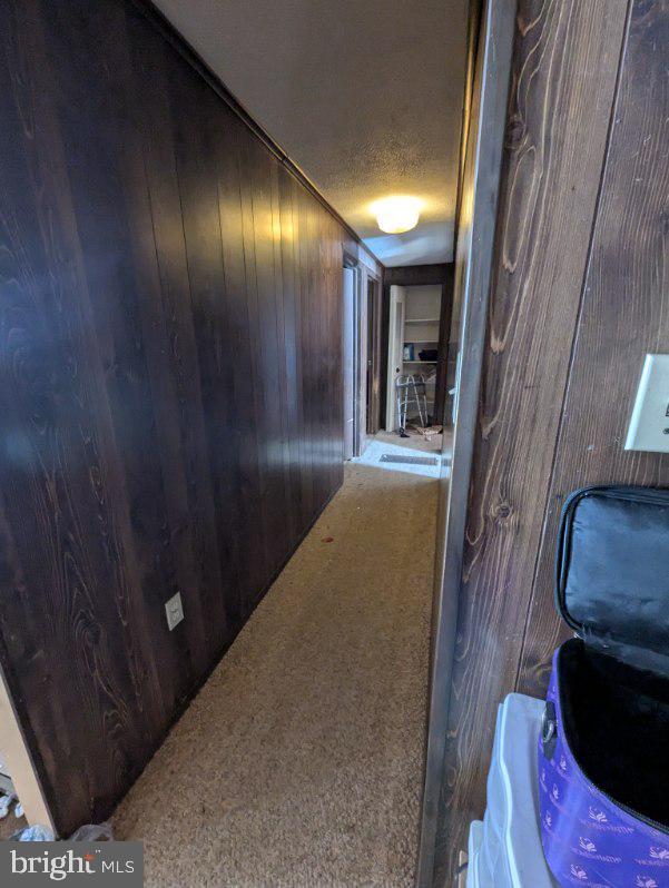 hall featuring carpet floors, wooden walls, and a textured ceiling