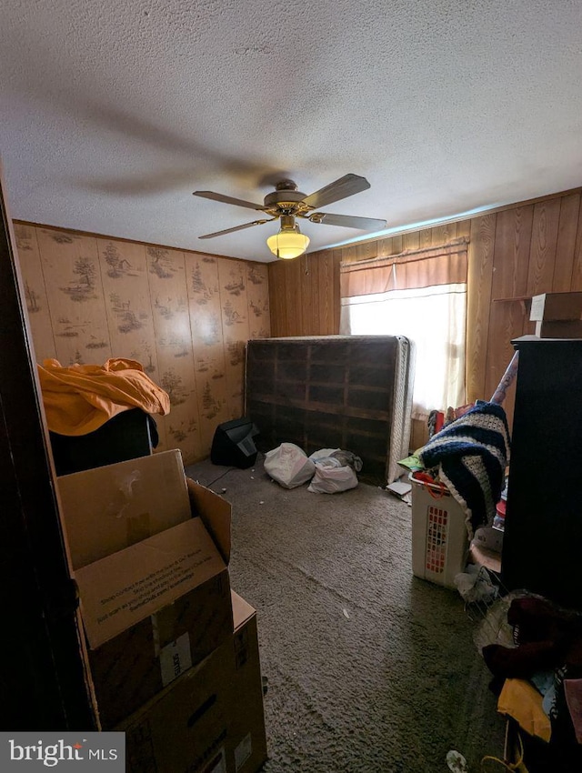 carpeted bedroom featuring wood walls, ceiling fan, and a textured ceiling