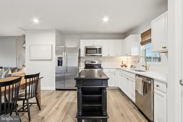 kitchen featuring stainless steel appliances, a sink, white cabinetry, light wood-style floors, and a center island