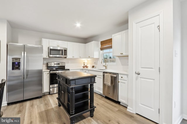 kitchen featuring light wood-style flooring, a sink, white cabinetry, appliances with stainless steel finishes, and a center island