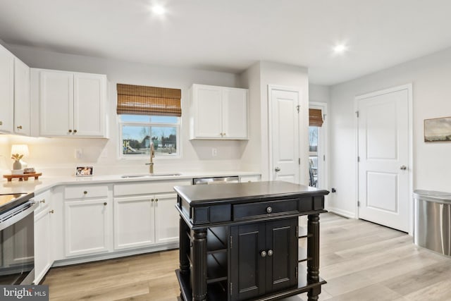 kitchen with white cabinets, dark cabinetry, a sink, and light wood-style flooring