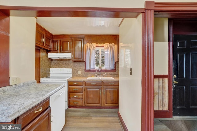 kitchen with light wood-style floors, brown cabinets, light countertops, under cabinet range hood, and a sink