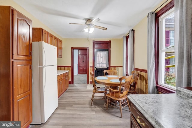 kitchen featuring a wainscoted wall, light countertops, freestanding refrigerator, ceiling fan, and light wood-type flooring