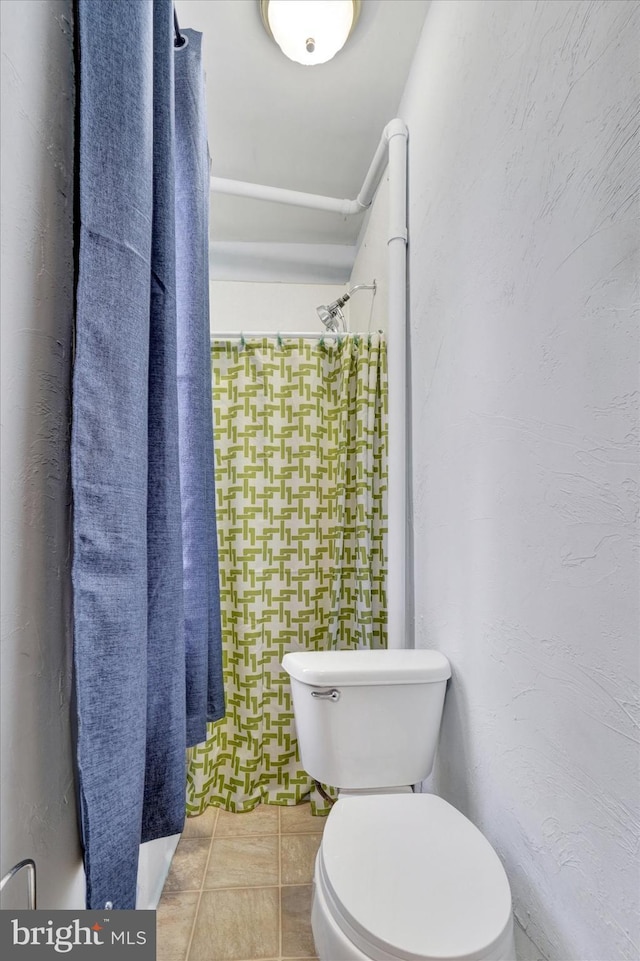 bathroom with tile patterned flooring, a textured wall, and toilet