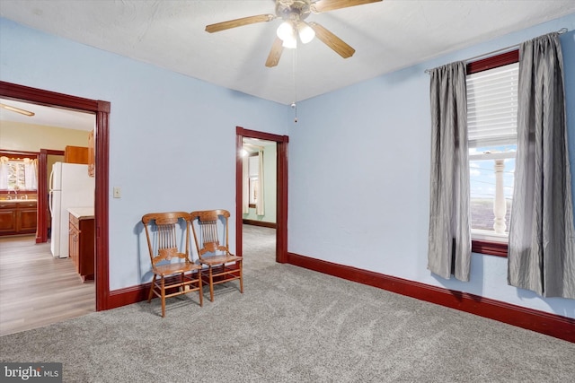 living area featuring baseboards, a ceiling fan, and light colored carpet