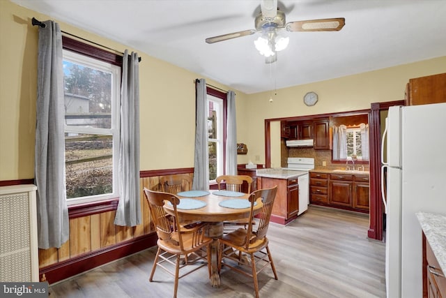 dining space with a wainscoted wall, light wood-style flooring, and ceiling fan