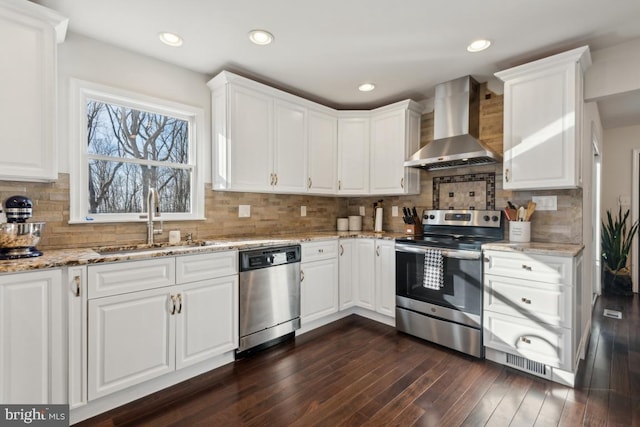 kitchen featuring dark wood-style floors, stainless steel appliances, white cabinetry, a sink, and wall chimney range hood