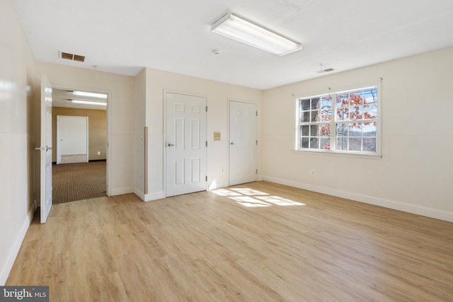 empty room featuring baseboards, visible vents, and light wood finished floors