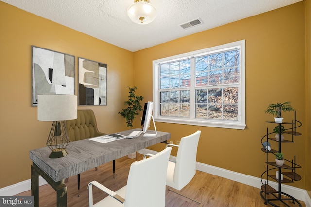 office space featuring a textured ceiling, wood finished floors, visible vents, and baseboards