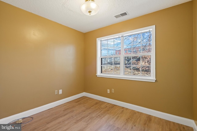 unfurnished room with a textured ceiling, light wood-style flooring, visible vents, and baseboards