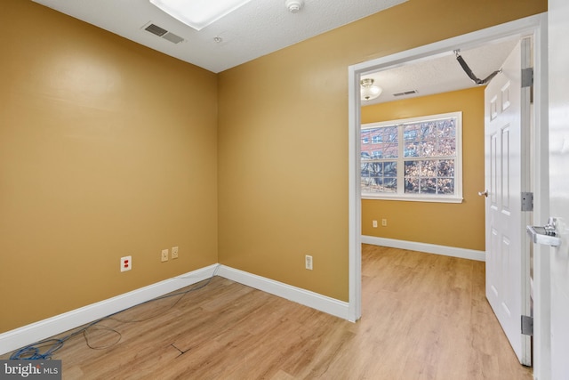 spare room with light wood-type flooring, visible vents, a textured ceiling, and baseboards