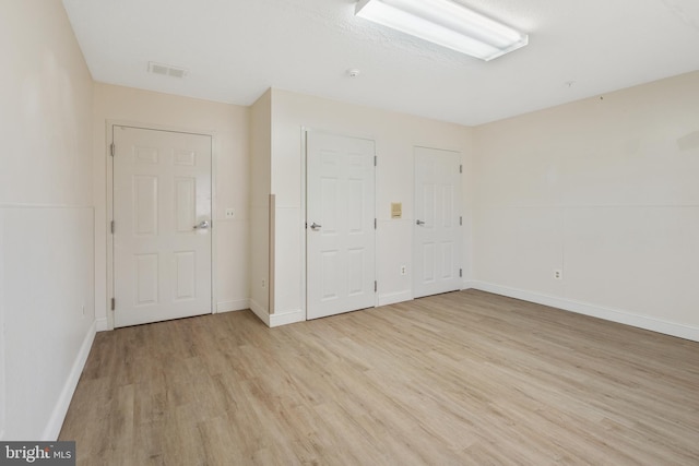 spare room featuring light wood-style floors, visible vents, and baseboards