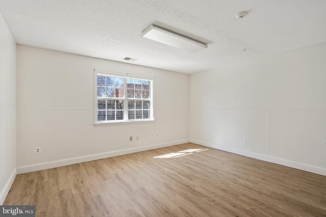 empty room with a textured ceiling, wood finished floors, and visible vents