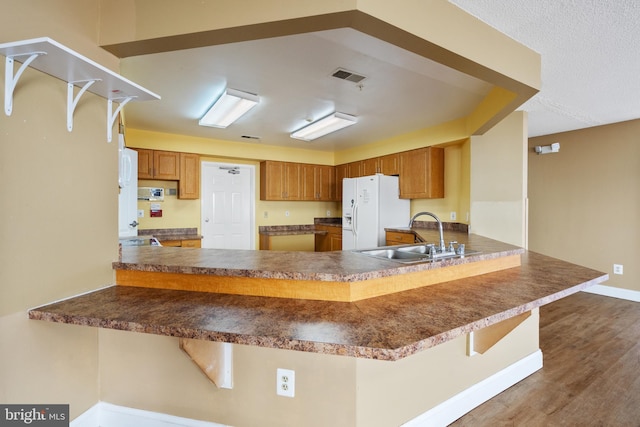 kitchen featuring white refrigerator with ice dispenser, visible vents, wood finished floors, a peninsula, and a sink