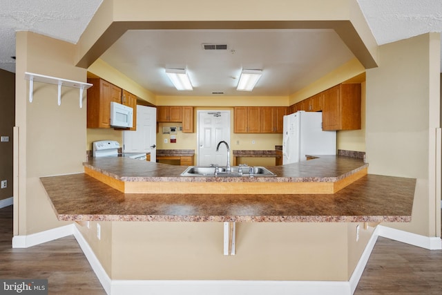 kitchen with dark wood-type flooring, white appliances, a sink, and a peninsula