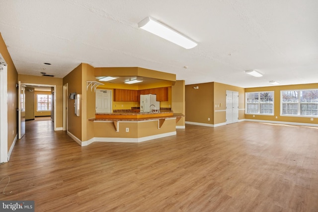 unfurnished living room with a textured ceiling, a sink, light wood-style flooring, and baseboards