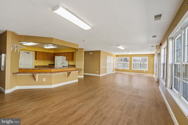 unfurnished living room with light wood-style flooring, visible vents, baseboards, and a textured ceiling