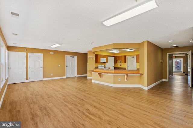 unfurnished living room with light wood finished floors, baseboards, and visible vents