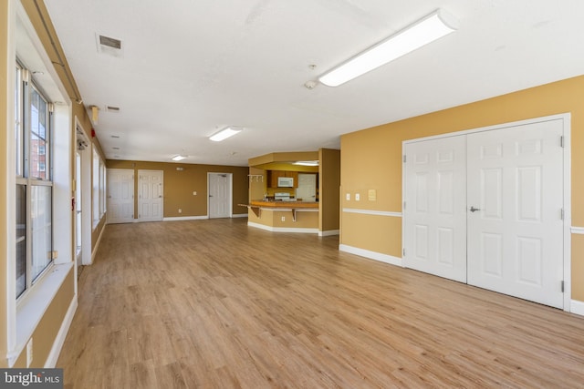 unfurnished living room with light wood-type flooring, visible vents, and baseboards