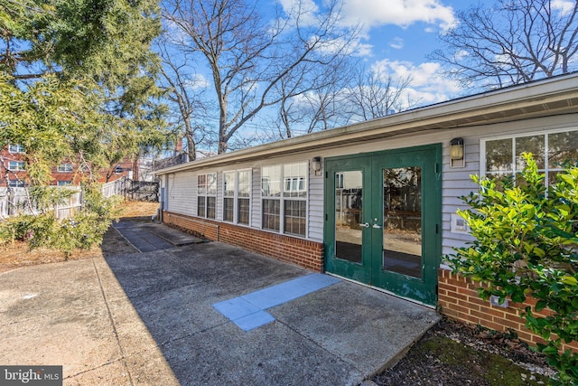 entrance to property with a patio area, french doors, brick siding, and fence