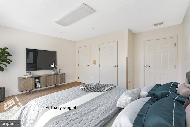 bedroom with baseboards, visible vents, and wood finished floors