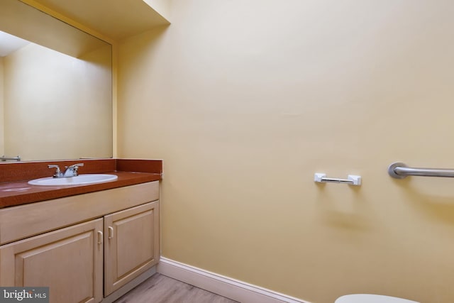 half bathroom featuring toilet, wood finished floors, vanity, and baseboards