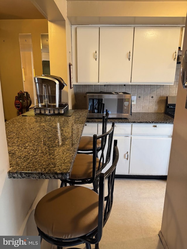 kitchen featuring dark stone counters, white cabinets, stainless steel microwave, and backsplash