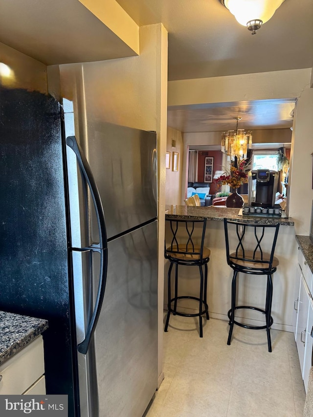 kitchen with a chandelier, freestanding refrigerator, white cabinets, and dark stone counters