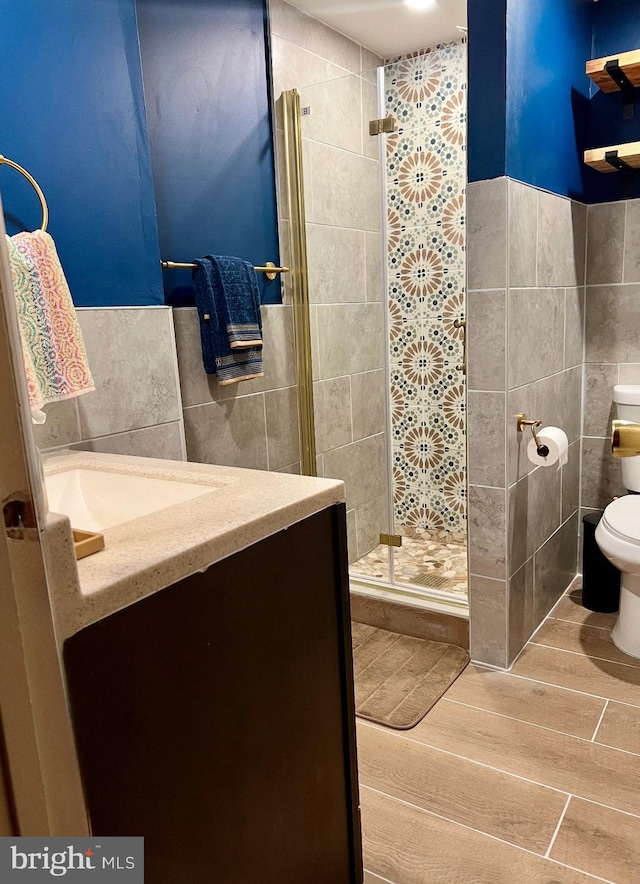 full bath featuring toilet, wood finish floors, vanity, tile walls, and a shower stall