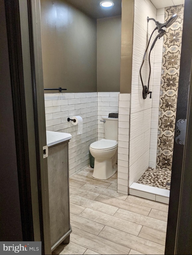 full bath featuring a stall shower, toilet, a wainscoted wall, wood tiled floor, and tile walls