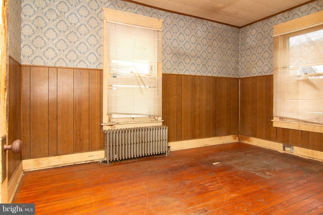 empty room featuring radiator, wallpapered walls, crown molding, and a wainscoted wall