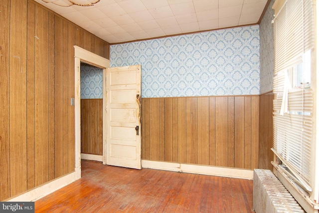 unfurnished room featuring hardwood / wood-style flooring, wainscoting, wood walls, and wallpapered walls