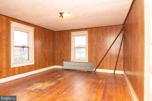 unfurnished room with radiator, wood walls, plenty of natural light, and wood-type flooring