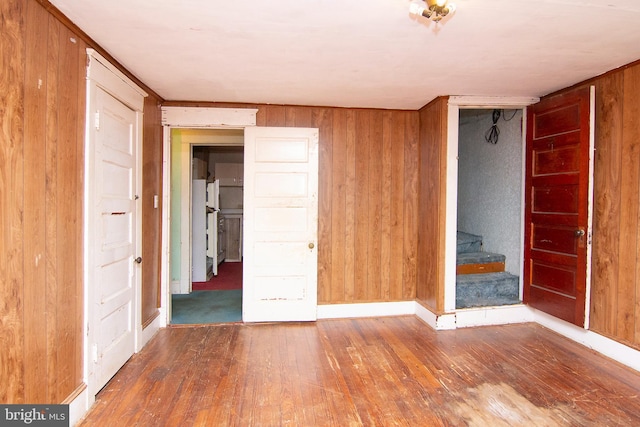 unfurnished room featuring stairs, wood walls, hardwood / wood-style flooring, and baseboards