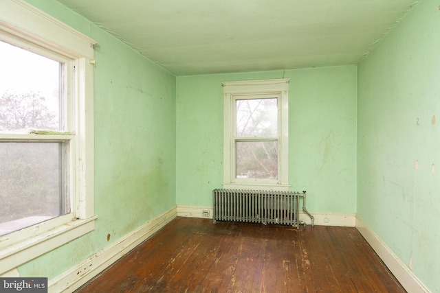 spare room featuring wood-type flooring, baseboards, and radiator heating unit