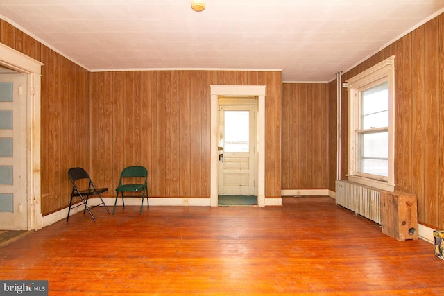 unfurnished room with ornamental molding, radiator heating unit, wood finished floors, and wooden walls