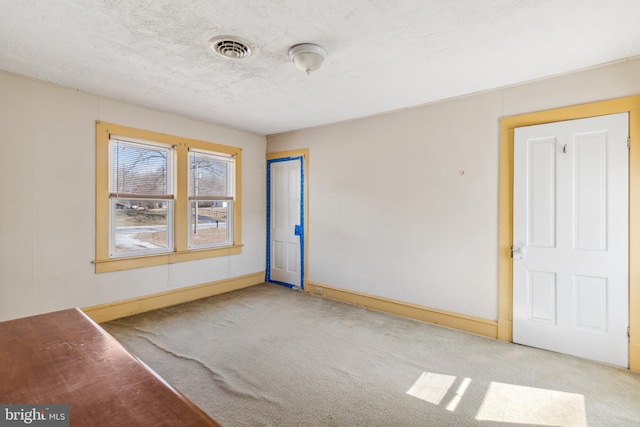 carpeted empty room featuring baseboards, visible vents, and a textured ceiling