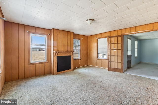 unfurnished living room featuring carpet floors, a wealth of natural light, and wooden walls