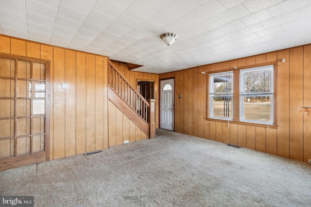 interior space with carpet floors, stairway, visible vents, and wooden walls