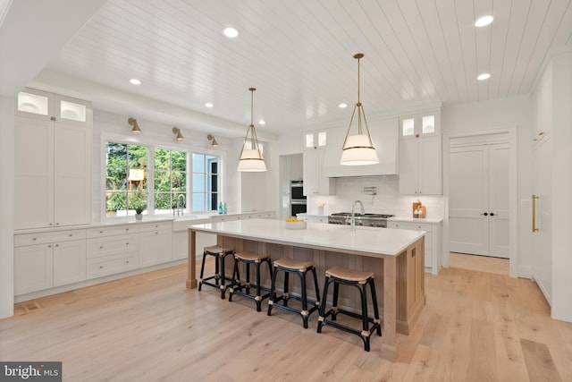 kitchen with stainless steel double oven, light countertops, a large island, light wood-type flooring, and tasteful backsplash